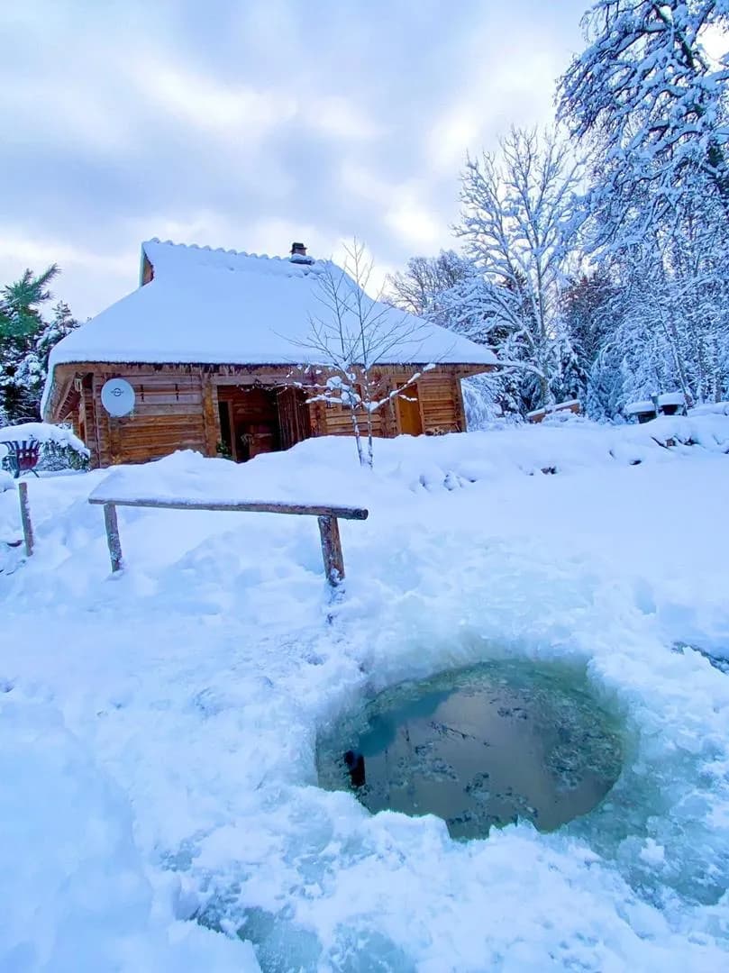 An ice hole cut in the pond before the sauna house on a frozen day, a handrail leading in