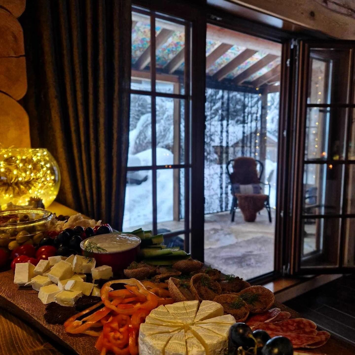 A winter spread of cheese and olives, snow beyond the glass doors