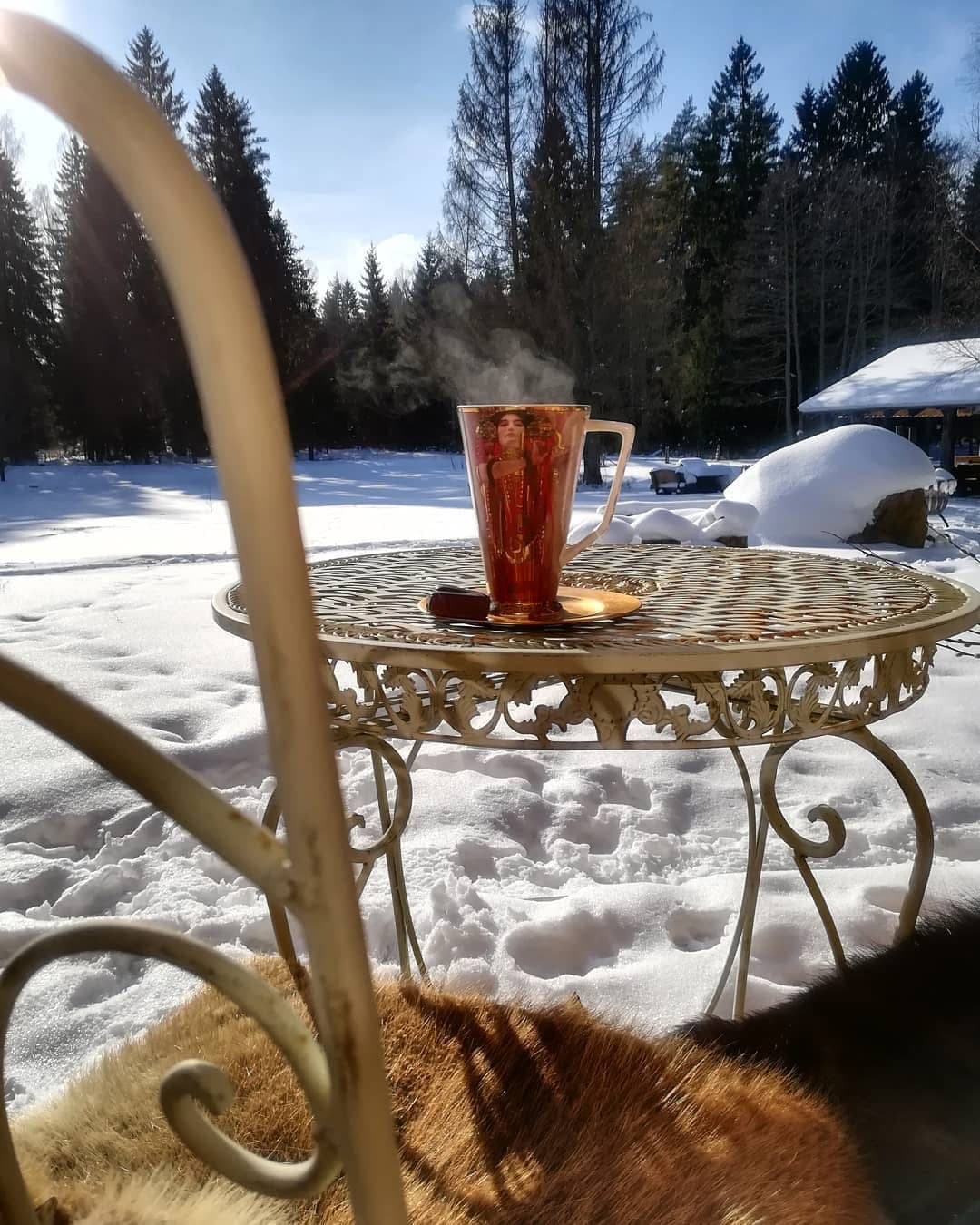 A steaming glass of tea on a wrought-iron table in the snow