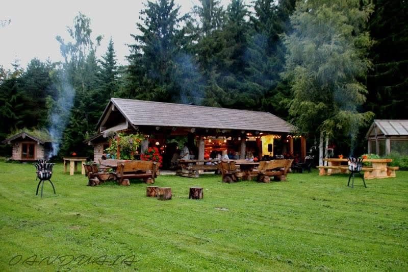 The outdoor kitchen at dusk, fire bowls smoking on the lawn