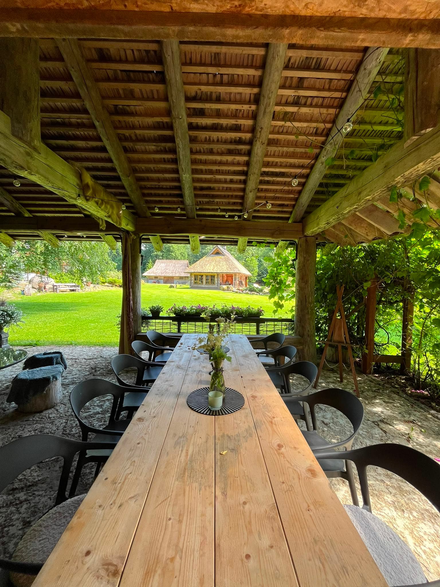The long timber table under the outdoor kitchen roof, lawn and house beyond