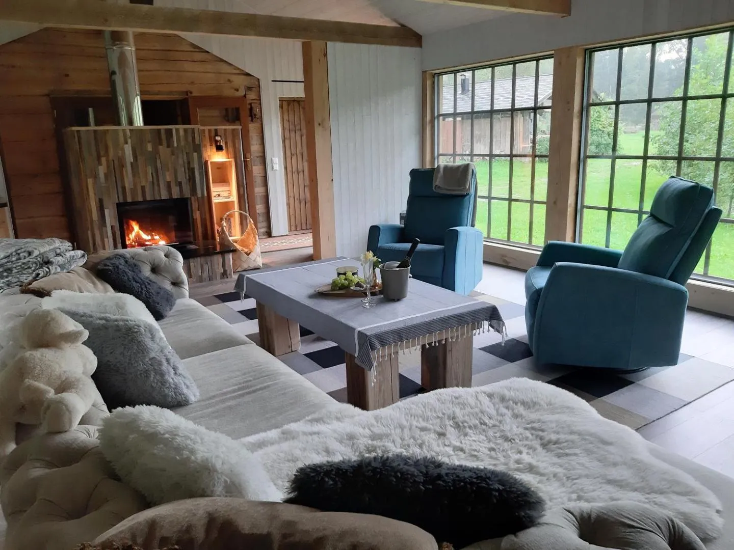Forest House — the living room with the fire lit, teal recliners at the window and wine on the table