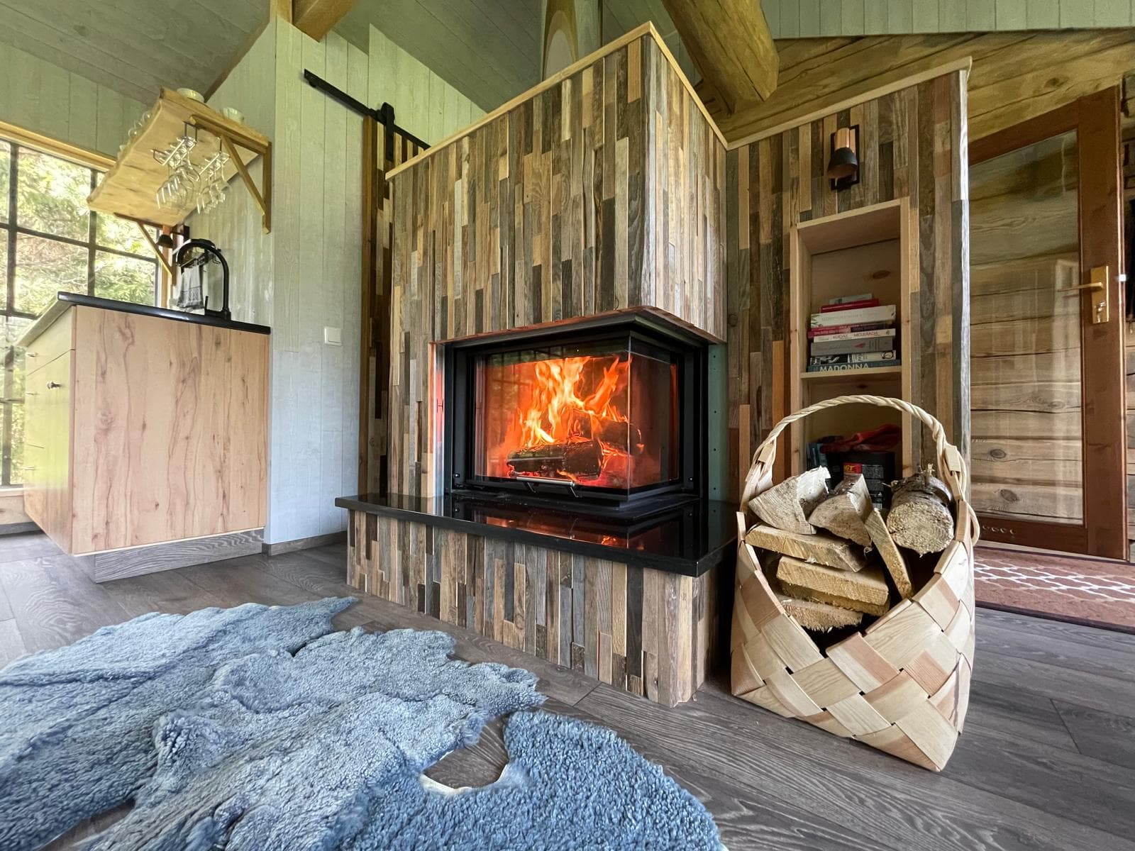 Forest House — the fireplace against its reclaimed-timber breast, a birch-bark basket of logs and a sheepskin on the floor