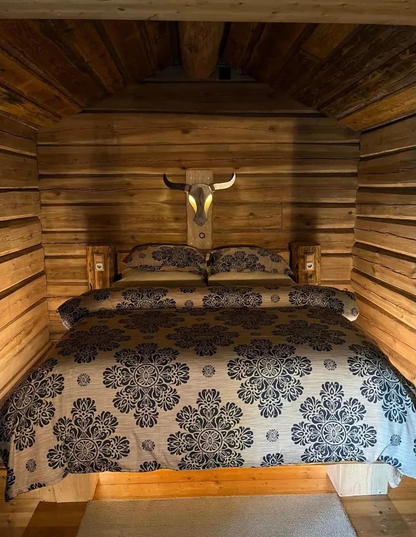 Forest House — the bed between the log walls, a lit bull’s head above the headboard