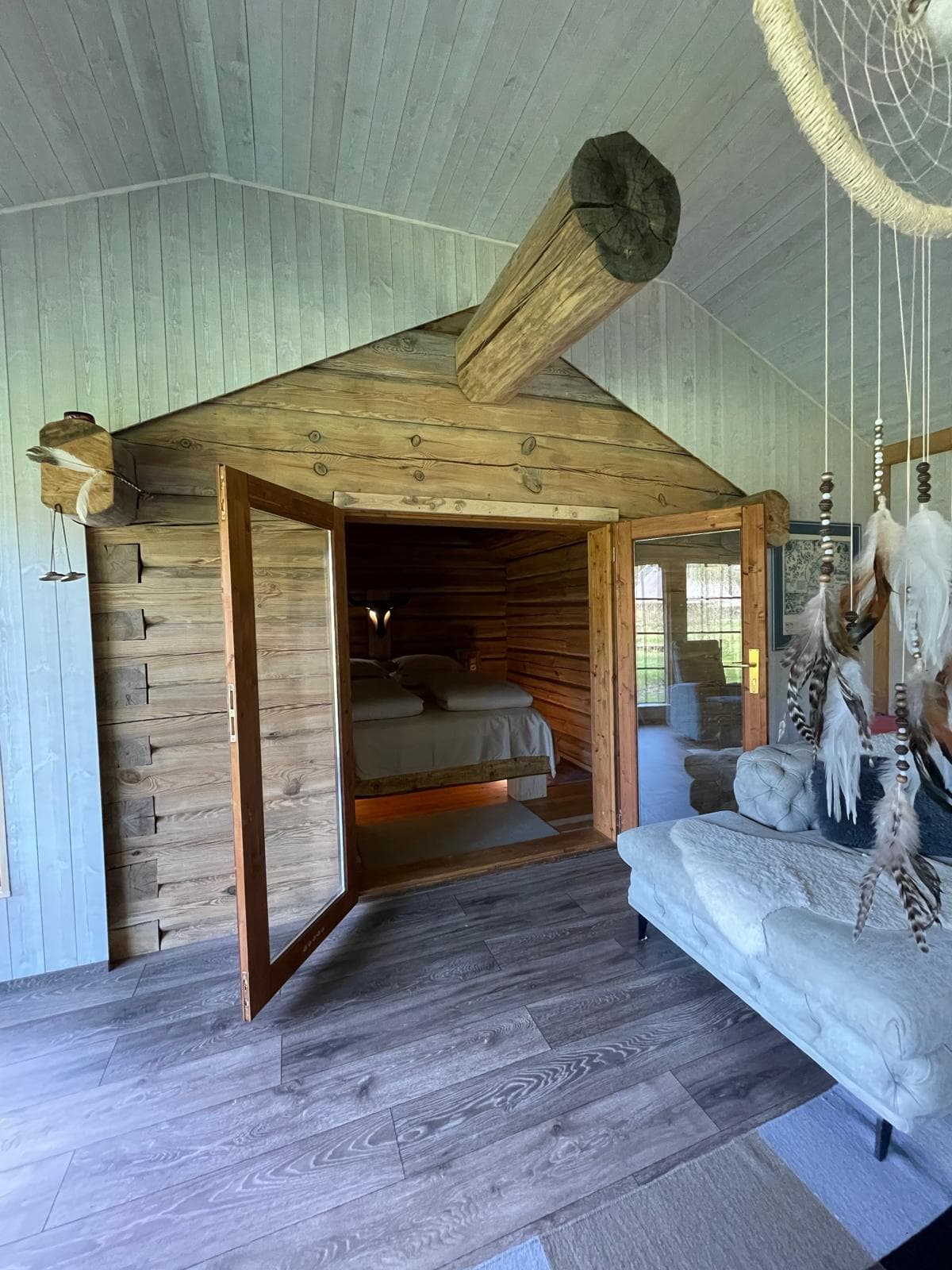 Forest House — the open door into the log-walled sleeping room, a dreamcatcher and sheepskins