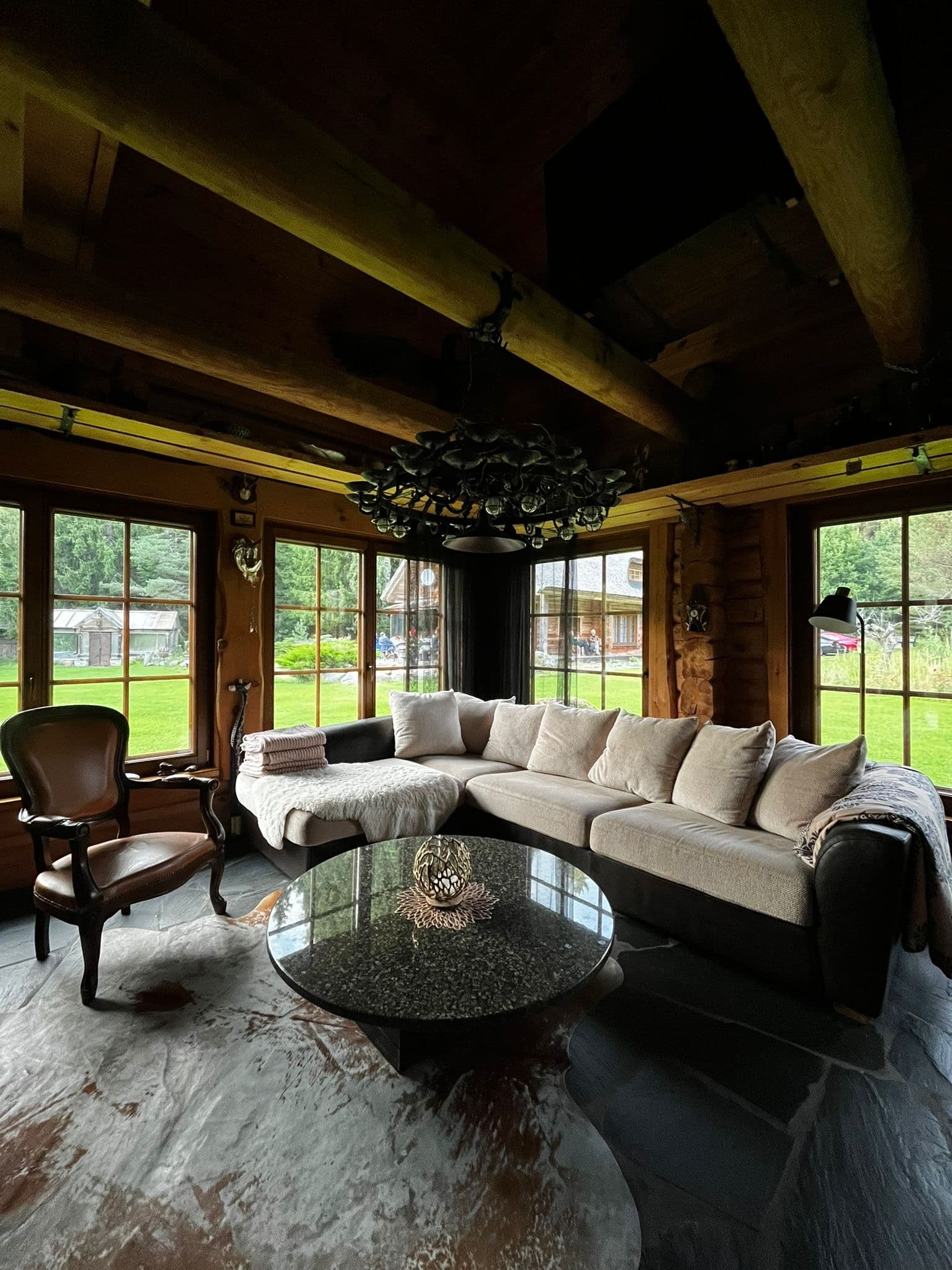 Sauna House — the living room under the oak-leaf chandelier, windows on three sides onto the lawn