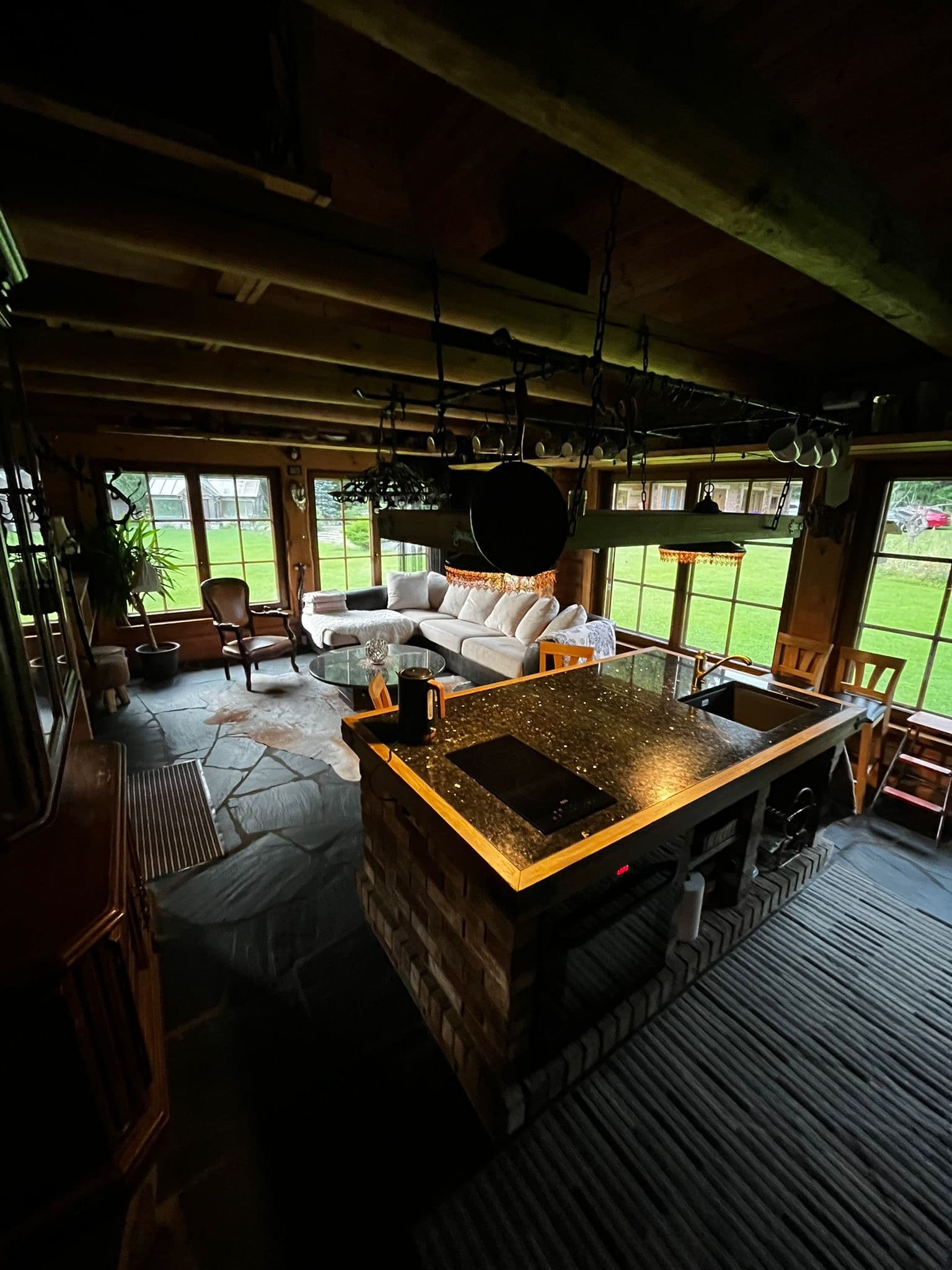 Sauna House — the kitchen island and the living room in one space at dusk, pots and mugs hung from the beam