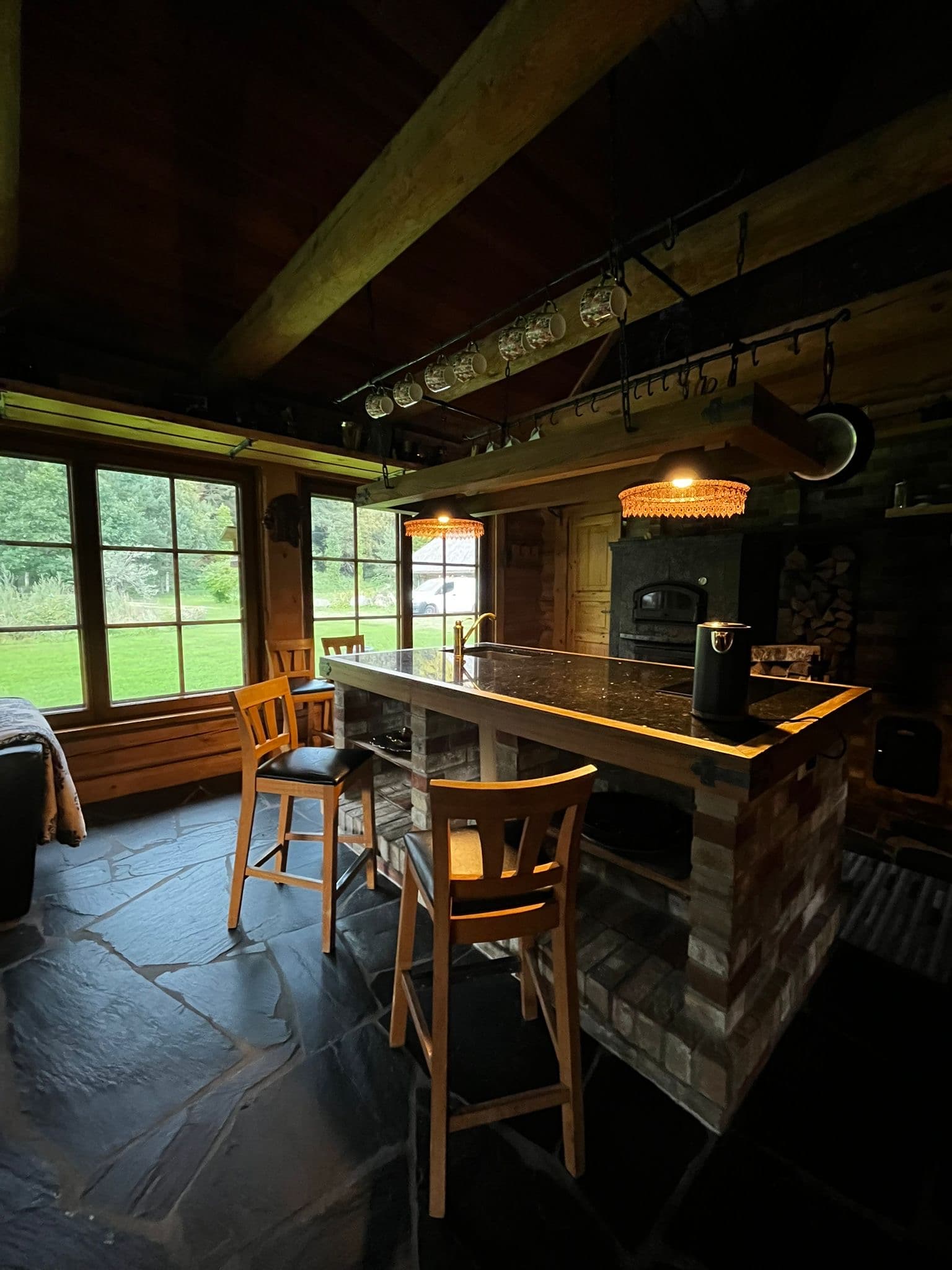 Sauna House — the kitchen island in the evening with bar stools, amber pendant lights and stacked firewood