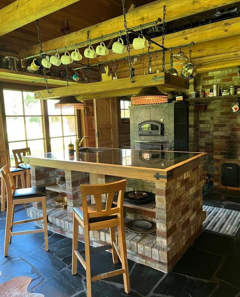 Sauna House — the kitchen island on a brick base, a wood-fired range and mugs hanging from the beam