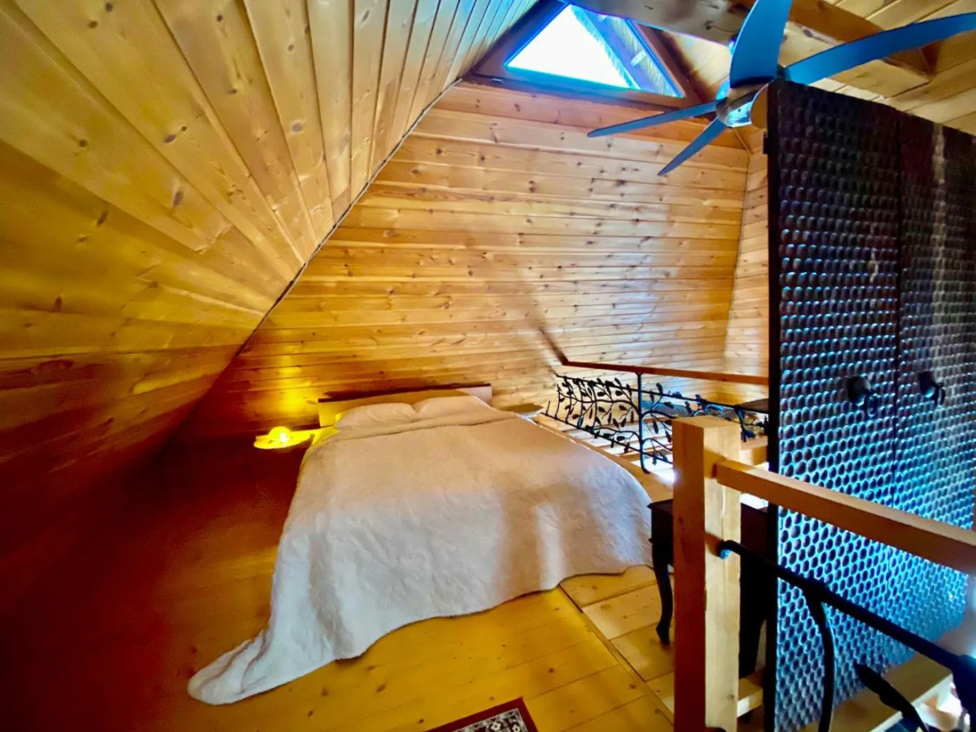 Sauna House — the loft bed under the roof slope, the forged railing and a ceiling fan