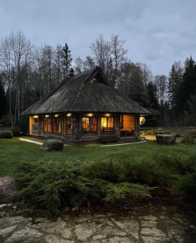 The Sauna House on an autumn evening, windows lit and the thatch gone mossy