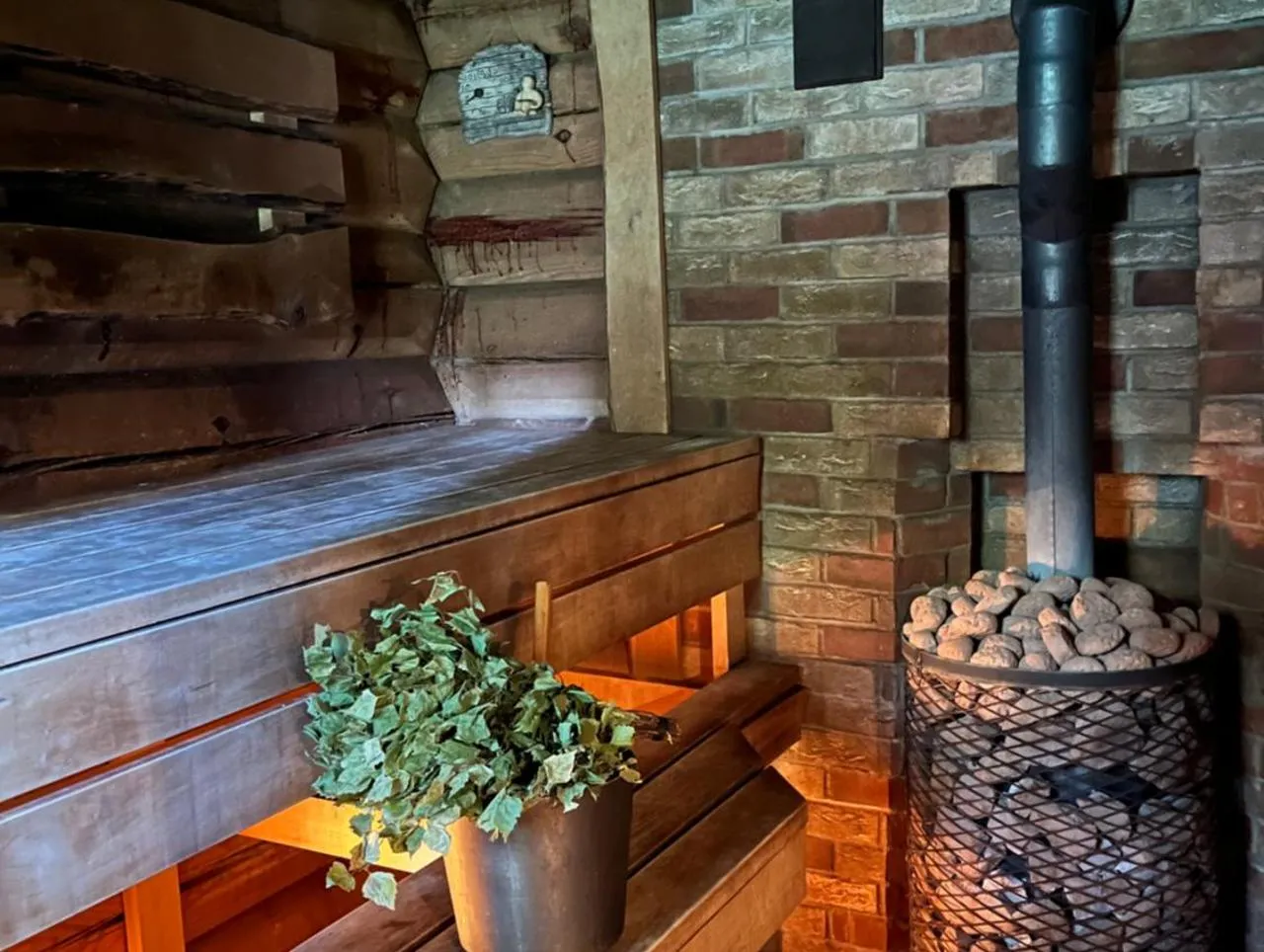 Sauna House — the steam room, hot stones on the stove and a birch whisk in a bucket beneath the bench