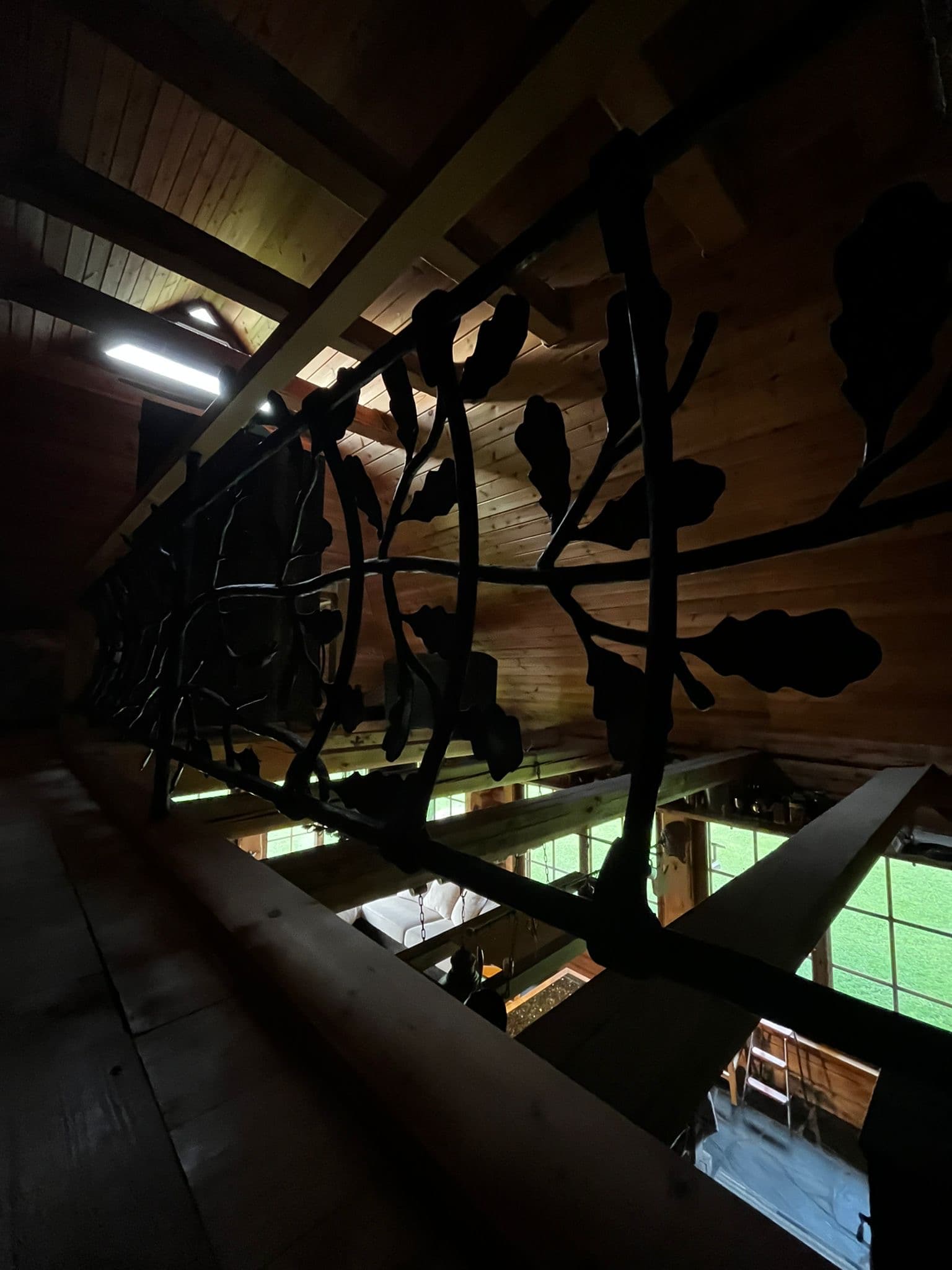 Sauna House — the forged oak-branch balustrade of the loft beneath the timber ceiling, the room below