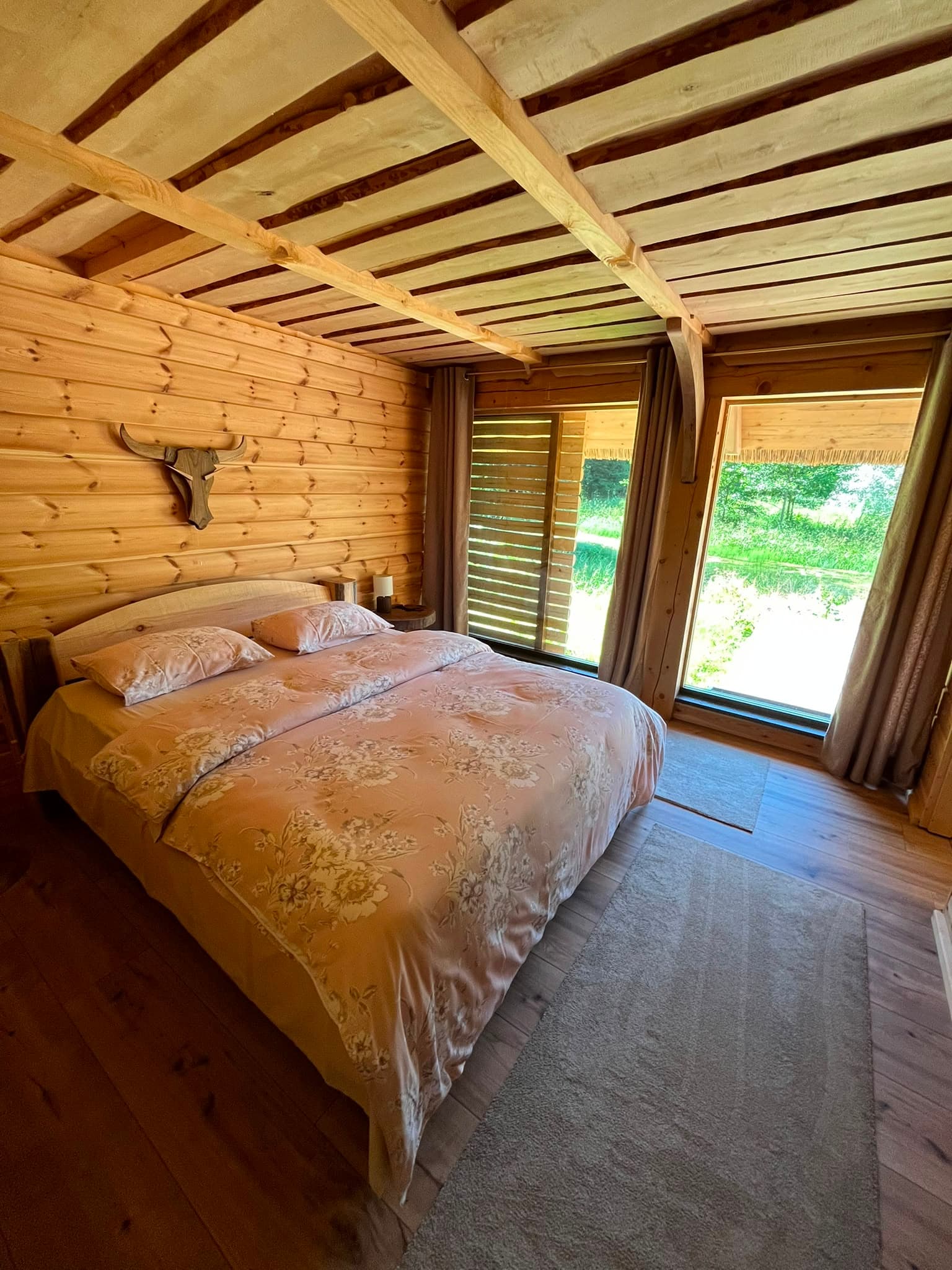 Pond House — the bedroom with floor-to-ceiling windows onto the meadow and a skull on the log wall