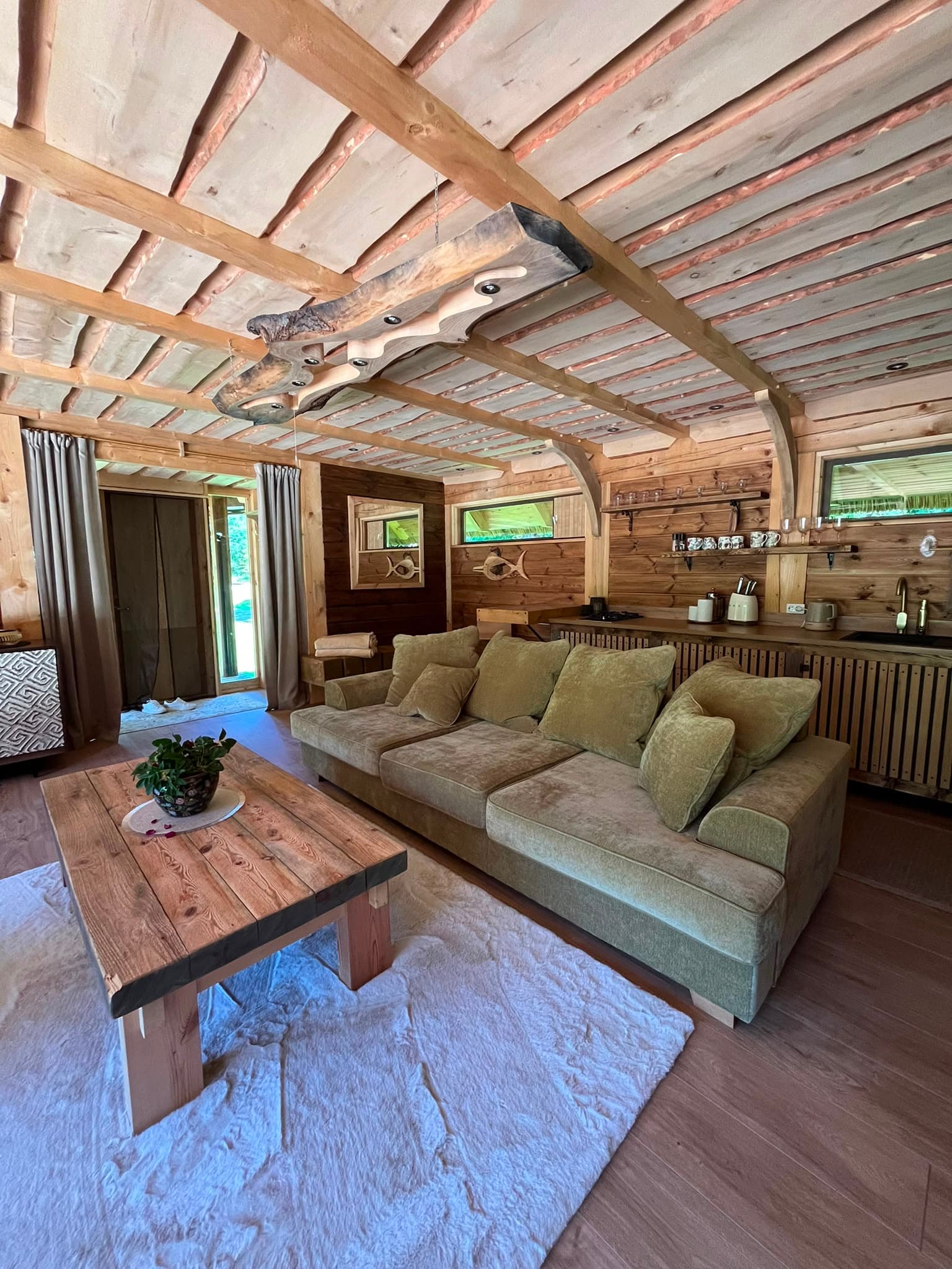 Pond House — the living room with its green sofa, carved roof beam and sheepskin rug