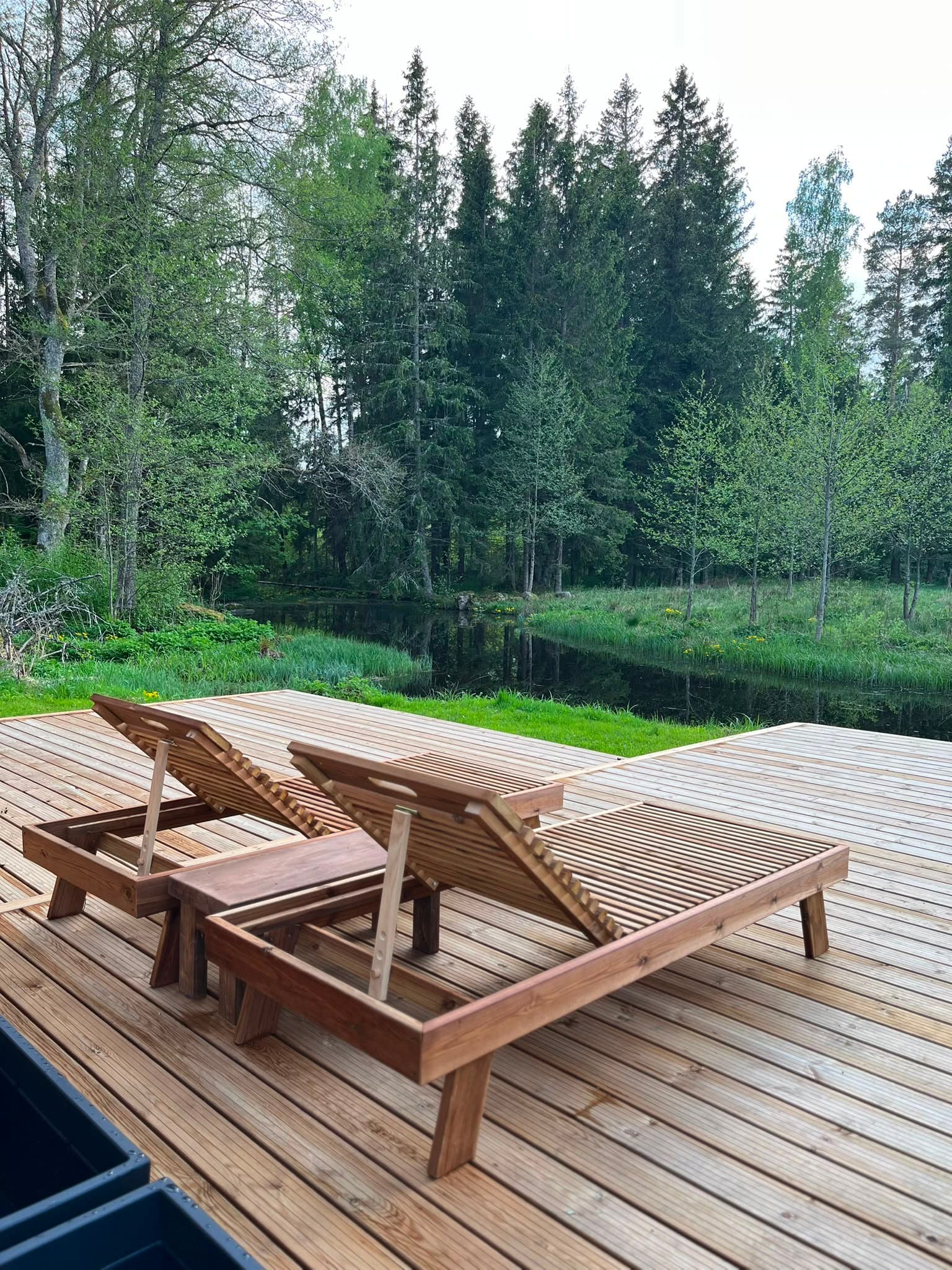 Pond House — two wooden loungers on the deck, the pond and the forest beyond them